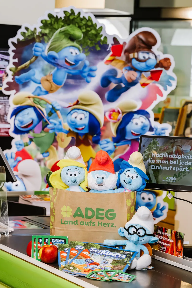 Originalfoto der ADEG-Schlümpfe-Alben auf einem Kassenband, mit Stickerpackungen und Plüschfiguren